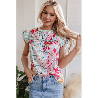 Women's spring floral top with white base, pink red yellow flowers, green striped ruffled sleeves, tucked into light-wash denim jeans
