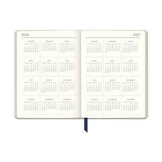 2027 navy dual-textured planner open spread showing 17-month calendar layout with cream paper and ribbon bookmark