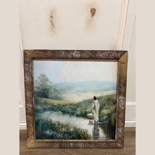 Rustic framed canvas of Jesus walking with lamb through water in pastoral landscape