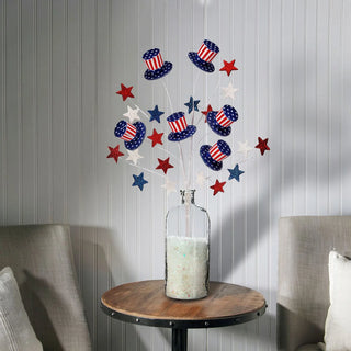 Decorative arrangement with red, white, and blue elements in a glass bottle on a wooden table against a gray wall.