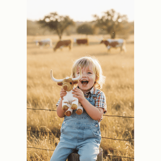 Child holding Larryy the Texas Longhorn plush outdoors