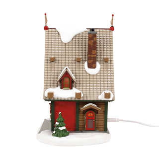 Department 56 Christmas village house with snow-covered roof and small Christmas tree