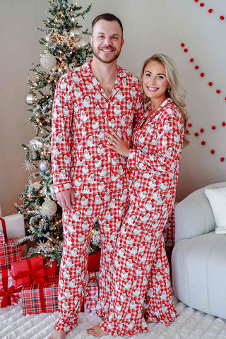 Couple wearing matching red plaid Santa Claus print Christmas pajama sets indoors near tree
