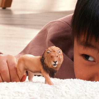 Child lying on white carpet playing with Schleich African Lion figurine up close