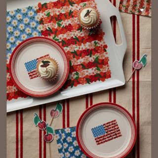 Fourth of July picnic setup with floral flag paper plates holding cupcakes and cherry toppers