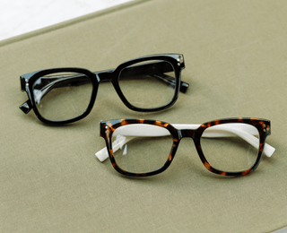 Peepers Aubrey reading glasses in black and tortoise frames displayed on a green book