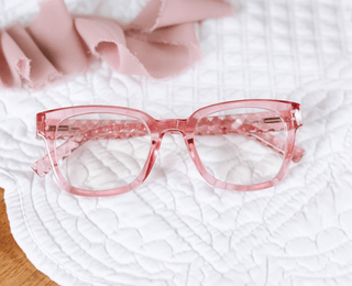 Aubrey Peepers pink transparent square eyeglass frames on white quilted fabric