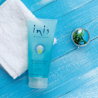 Tube of 'inis' bath and shower gel on a blue wooden surface with a towel and mirror.