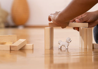 Schleich Bichon Frise figurine standing under wooden block arch on hardwood floor