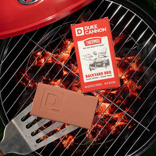 Duke Cannon Backyard BBQ Big Ass Brick of Soap on a lit charcoal grill with spatula