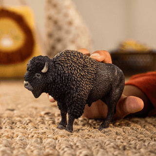 Schleich bison figurine held by a child's hand on a woven rug