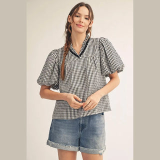 Close-up of black and white checkered women's top featuring scallop-trimmed V-neck detail