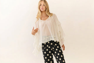 Black slim pants with large cream polka dots, modeled with a sheer white ruffle top
