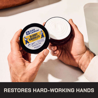 Hands holding open jar of Duke Cannon Bloody Knuckles Hand Balm showing white cream inside