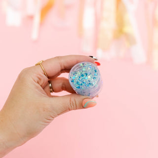 Hand holding clear jar of sky blue and royal blue glitter gel with chunky particles