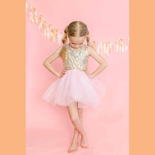 Blonde girl with blue iridescent glitter applied to scalp and hairline against pink backdrop