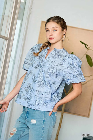Woman wearing a light blue floral blouse and jeans indoors.