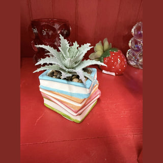 Colorful stacked book succulent pot with blue orange pink green spines and faux succulent on red wood