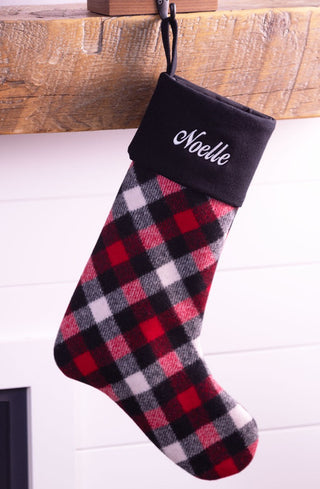 Personalized buffalo check Christmas stocking with black cuff embroidered with Noelle hanging on mantle