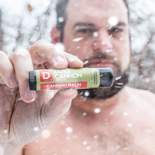 Man holding Duke Cannon Cannon Balm lip balm tube outdoors in falling snow