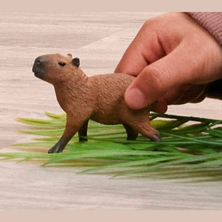 Small brown animal figurine on a grassy surface with a hand