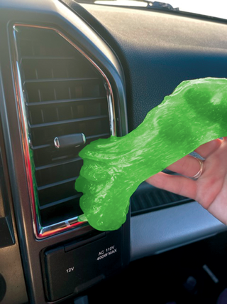 Hand holding green cleaning putty slime near car dashboard air vent