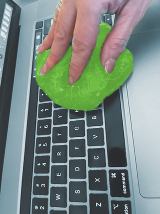 Green cleaning putty slime pressed onto a laptop keyboard by a hand