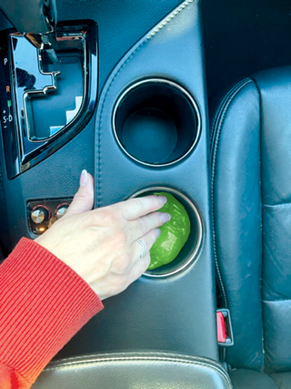 Green cleaning putty slime pressed into car cup holder by hand