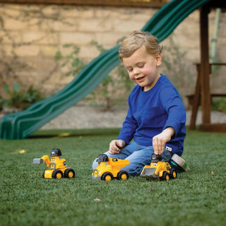 Child playing with yellow CAT excavator dump truck and loader toys on outdoor grass