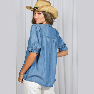 Women's light blue chambray ruffle shirt back view with smocked cuffs and curved hem
