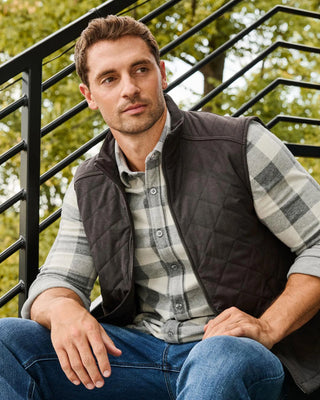 Man wearing dark gray quilted vest over gray plaid flannel shirt and jeans