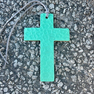 Mint green cheetah print cross pendant on gray leather cord, gravel background