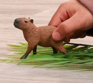 Small brown animal figurine on a grassy surface with a hand