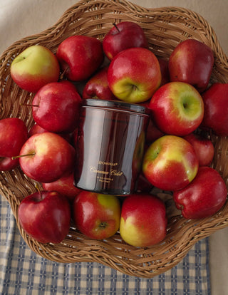 Fall-themed Aromatique Cinnamon Cider candle displayed with fresh apples in wicker basket