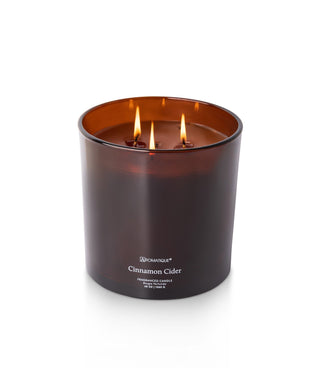 Aromatique Cinnamon Cider 48oz three-wick candle in amber brown glass vessel with lit flames