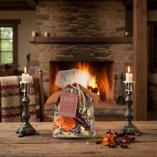 Aromatique Cinnamon Cider decorative fragrance bag displayed on rustic wooden table beside lit candles and fireplace.