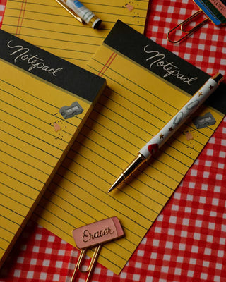 Two yellow Class Notes notepads by Rifle Paper Co. styled with a pen and eraser clip on red gingham