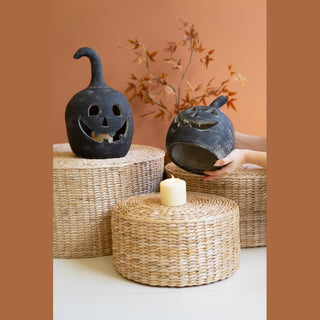 Dark blue clay jack-o'-lanterns with carved faces displayed on woven baskets with candle