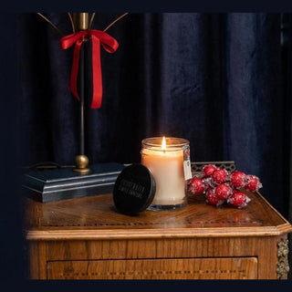 Lit Bridgewater apple spice candle on antique nightstand with frosted berries and navy velvet curtain