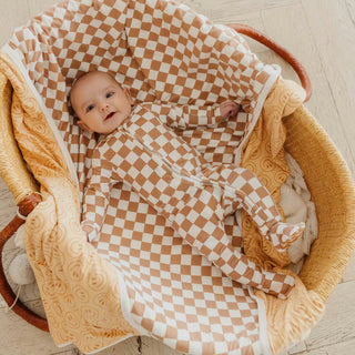 Tan white checkerboard baby footie pajamas worn by baby in bassinet