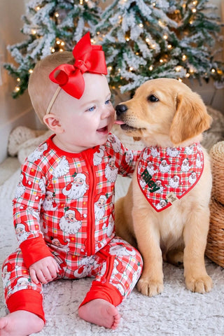 Baby girl in Caden Lane Cozy Claus Santa plaid zipper romper smiling with golden retriever puppy