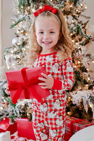 Young girl smiling in red plaid Santa Claus bamboo Christmas pajama set holding gift