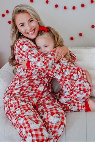 Mother and daughter wearing matching red plaid Santa Claus print bamboo pajama sets while hugging on a couch