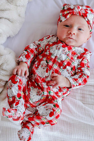 Baby wearing Caden Lane Christmas zipper footie with Santa Claus plaid print and matching headband bow.