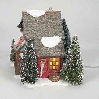 Department 56 lighted village building with snow-dusted miniature evergreen trees surrounding red cottage