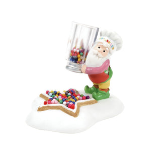 Department 56 elf figurine pouring colorful sprinkles onto a star-shaped cookie decoration