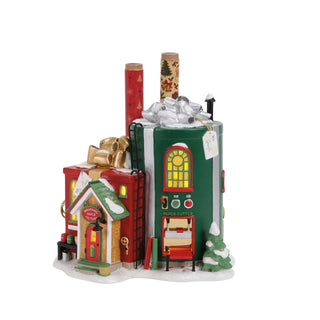 Department 56 Wrapping Paper Factory North Pole Village building with green gift box tower, red annex, and illuminated yellow windows