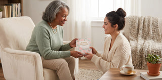 Woman gifting My Favorite Bible Verse Devotional book with pink floral cover to older woman in cozy living room