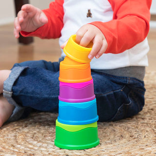 Toddler stacking rainbow-colored Dimpl Stack cups by Fat Brain Toys while sitting on floor.