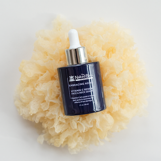 The Naked Bee Vitamin C Renew Face and Neck Serum in dark navy dropper bottle on natural sea sponge